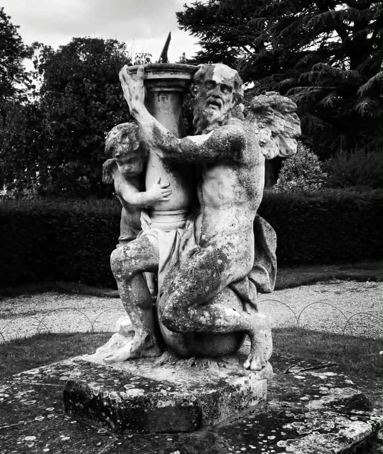 A black and white photo of a sundial statue with Father Time and a cherub