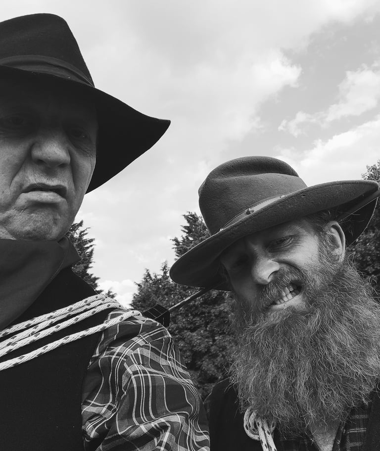 Two men wearing vintage cowboy hats and western attire in a black and white portrait.