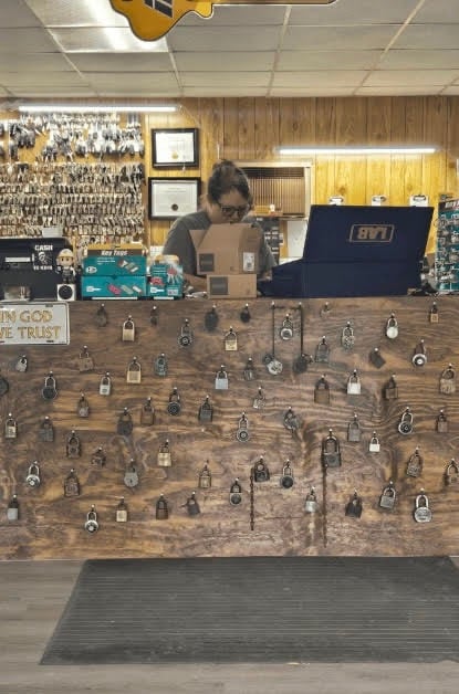 Emily, a female locksmith, assisting customers at the front counter of Jack's Locksmith in Burnsville, NC, wall of locks