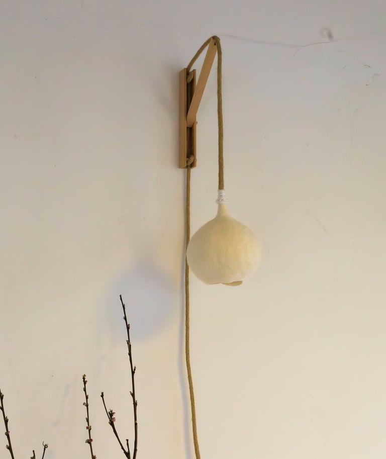 Handgemaakte vilten wandlamp Luminosa in maat S, bevestigd aan een houten houder.