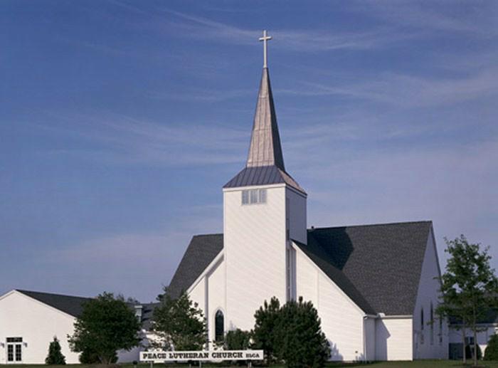 Peace Lutheran Church building featuring a white exterior with a tall steeple against a clear blue sky.