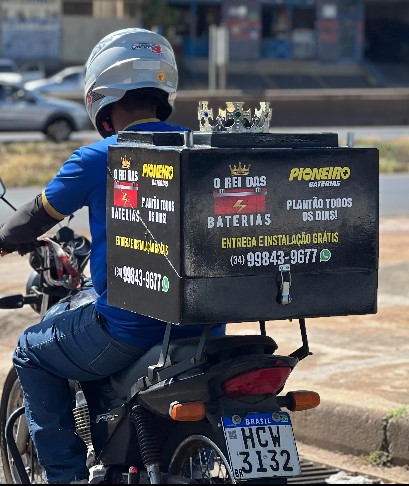 Um entregador segura uma bateria da Disk Baterias Uberlândia em frente a um carro amarelo.