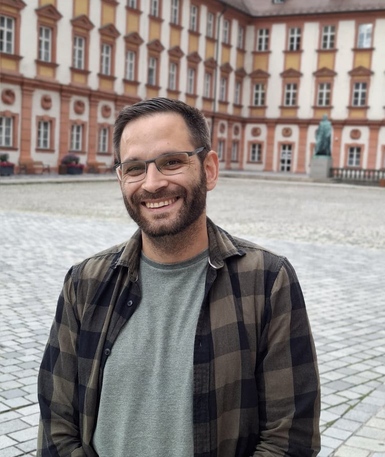 Inhaber, Patrick Angerer der freundlich in die Kamera guckt und in Bayreuth steht im Hintergrund altes Schloss in Bayreuth