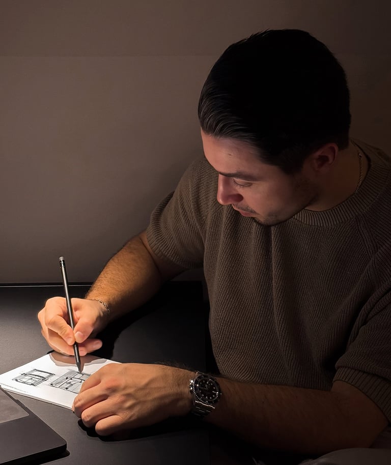 A designer sketching with a pencil at a dark desk.