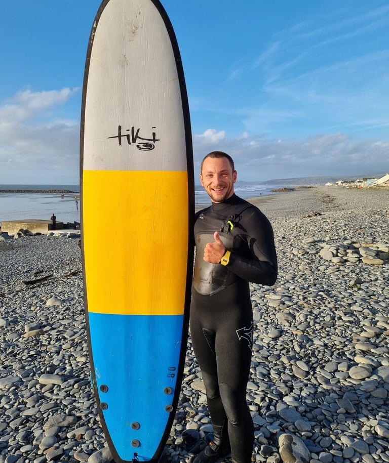 Surf coach Matt, holding a Tiki Grizzly surf board and giving the thumbs up