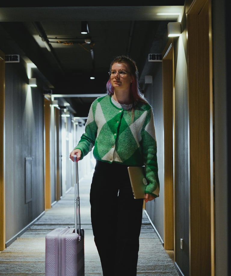 Una chica con un ordenador portátil y una maleta en el pasillo del hotel.