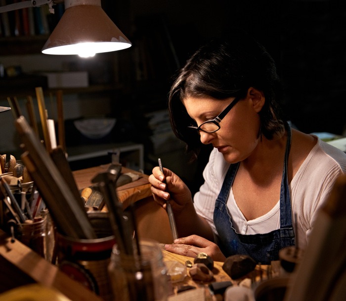 mujer de lentes sosteniendo herramienta de joyeria artesanal en area de trabajo