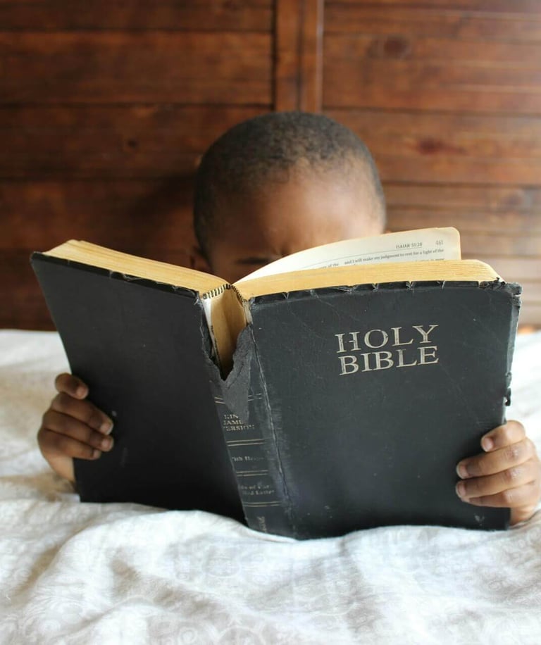 a young boy is reading a book while holding a bible