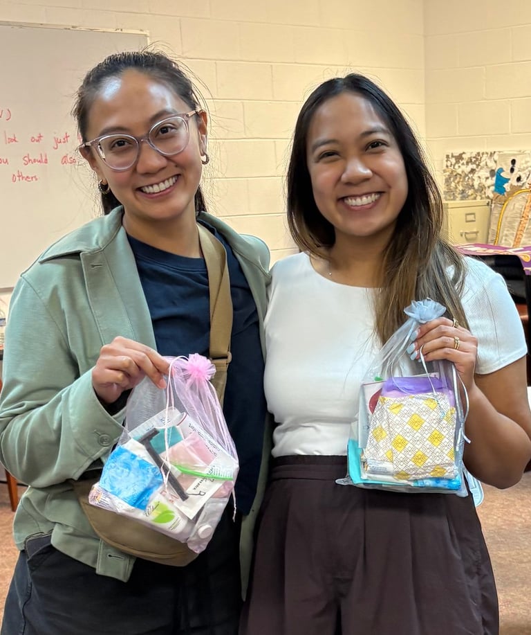 two women standing next to each other in a room holding hygiene kits