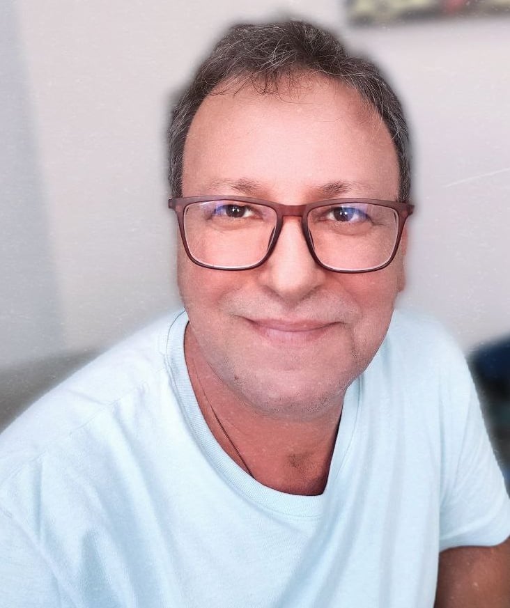 Foto do Ourives, Edno Oliveira, ele está de camisa azul, óculos e sorrindo.