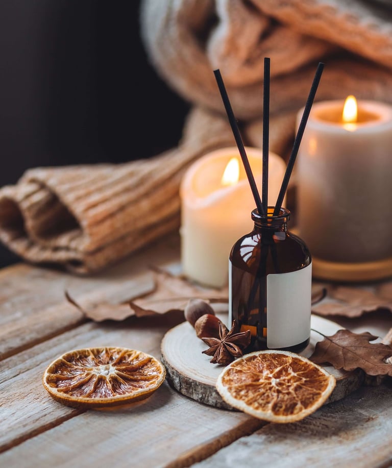 Cozy autumn flat lay with lit candles, amber glass reed diffuser, dried orange slices, star anise, a