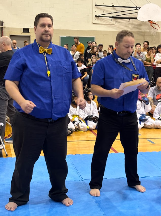 two men standing on a blue mat with a man in a blue shirt