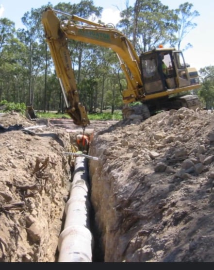 Yellow excavator digging a deep trench for underground pipe installation