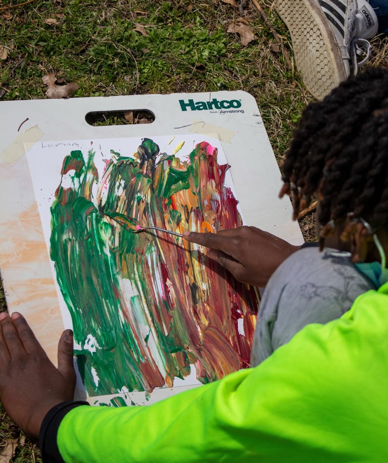 Young boy using a palette knife to smooth paint dabs over a paper.