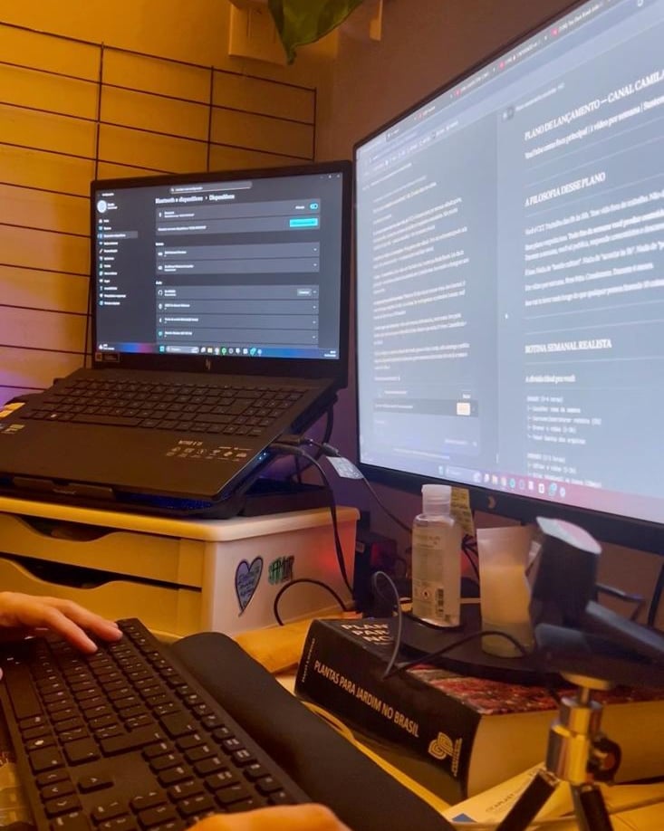 Dual monitor home office setup with a laptop, keyboard, and Brazilian flag on the wall.