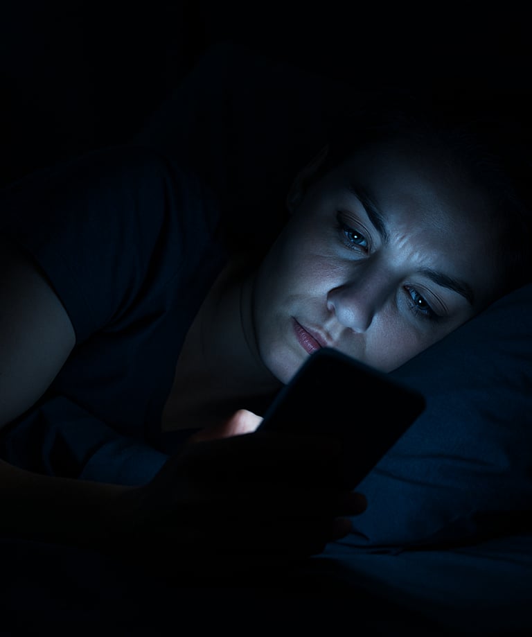 Realistic woman in bed in a dark room with her phone screen lighting up her face blue dimly