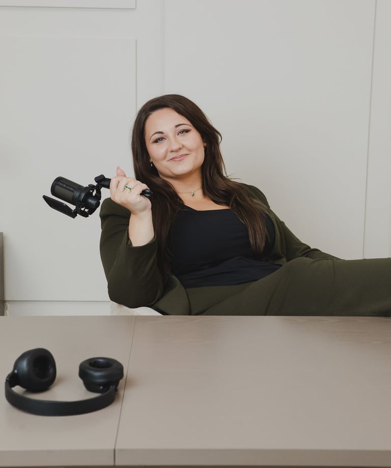 Adriana a podcaster in an olive blazer holding a microphone at her studio desk with headphones.