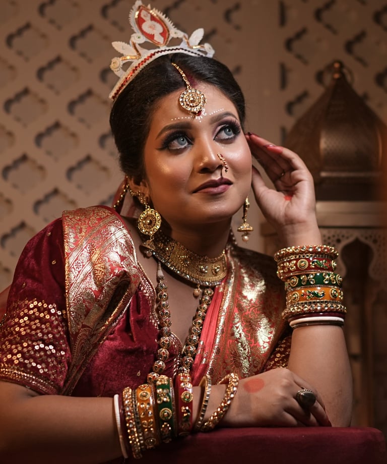 Bengali bride in red saree with bold kohl eyes, gold jewelry, chandan forehead design, and tradition