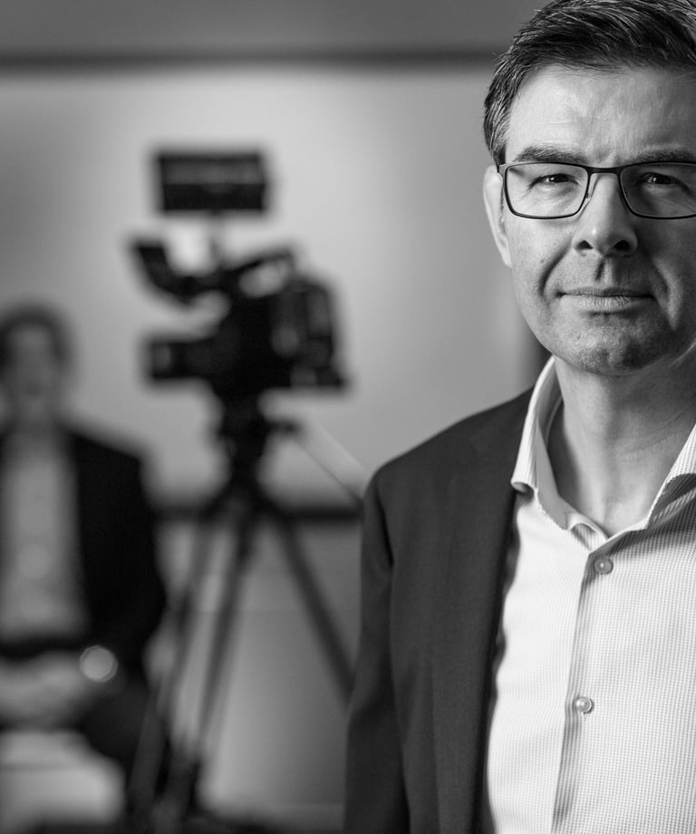 a man in a suit and glasses is standing in front of a camera