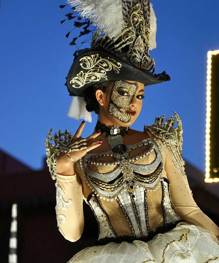 Woman in an ornate gold and white carnival costume with a skull face mask and feathered hat.