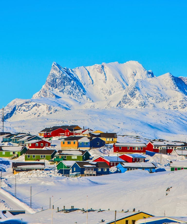 Colorful houses in a snow-covered Greenland village below a majestic arctic mountain peak.