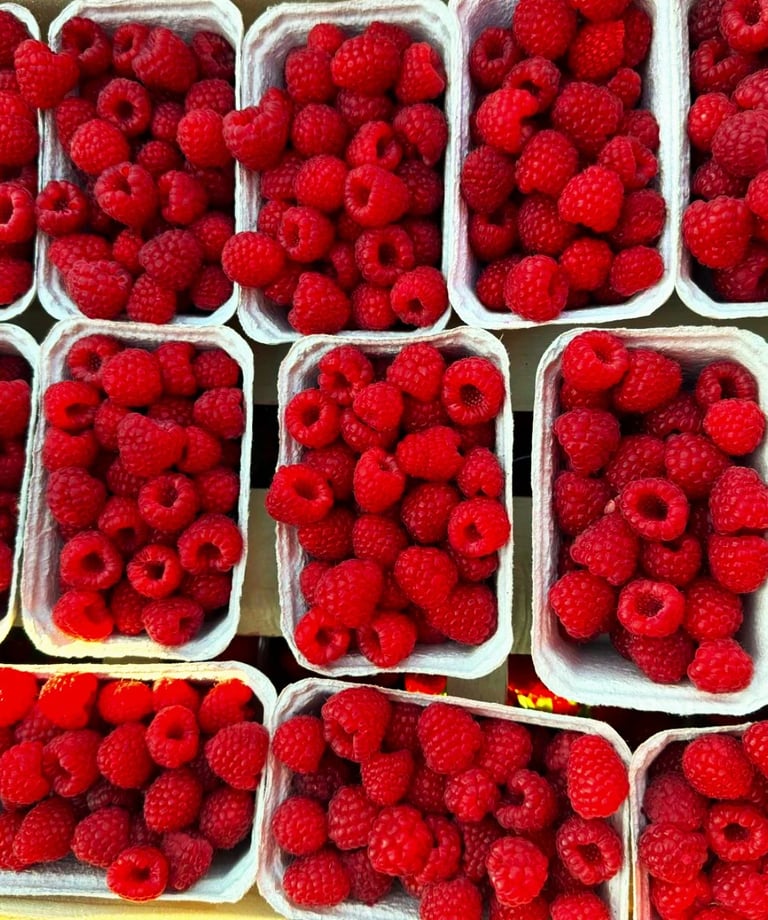 Świeże maliny w plastikowych pojemnikach, gotowe do sprzedaży na targu.