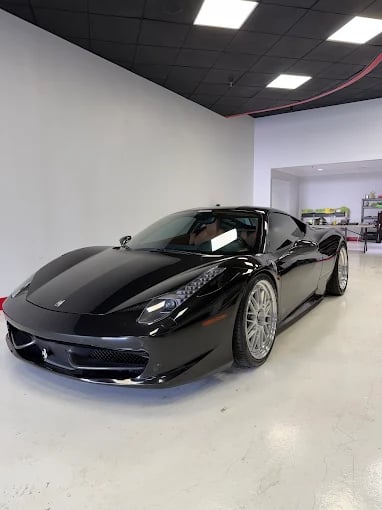 A sleek black Ferrari 458 Italia supercar with silver multi-spoke wheels parked in a luxury automotive showroom.