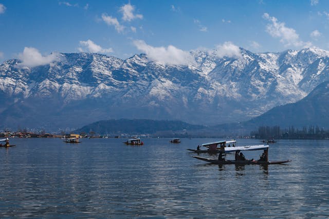 Shikara boats floating on Dal Lake with the snow-covered Himalayan mountains of Kashmir in the background.