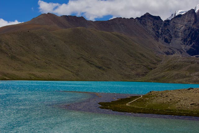 Turquoise high-altitude alpine lake nestled beneath rugged Himalayan mountain peaks under a blue sky.