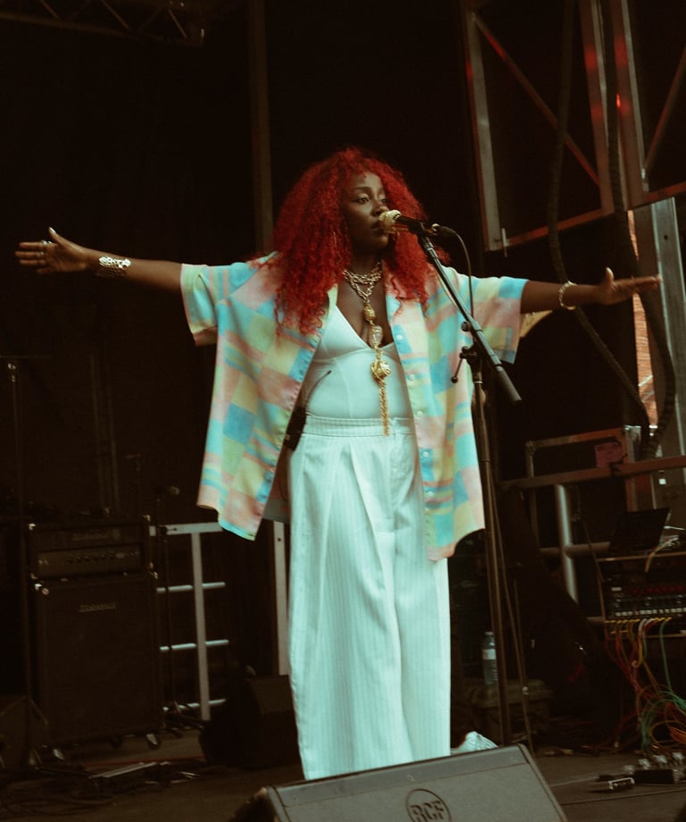 A female singer with vibrant red hair performs live on stage wearing a colorful patterned shirt.