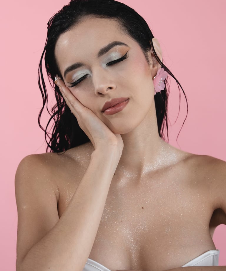 Woman with wet hair and silver glitter makeup posing against a pink background.