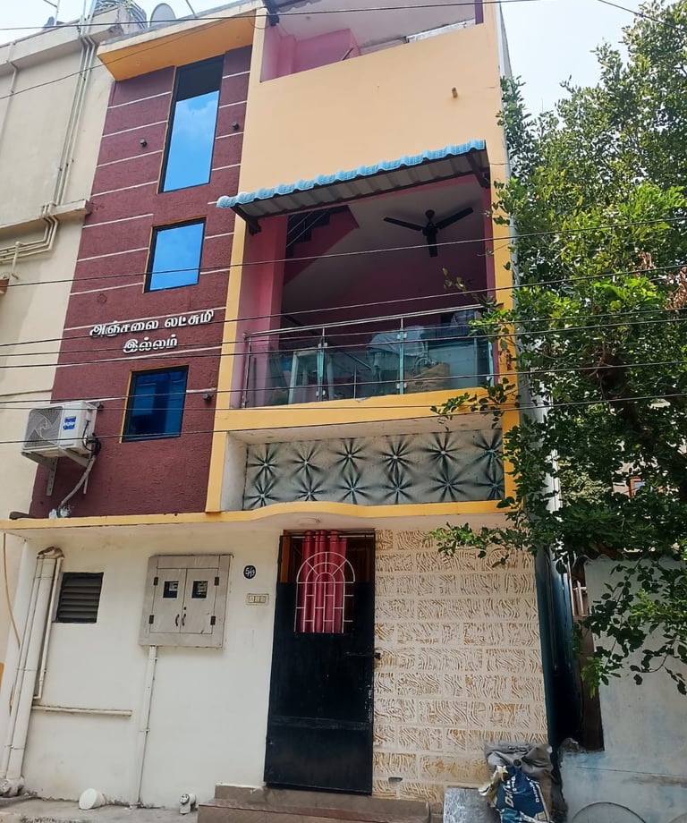 Three-story residential building with a balcony, yellow and maroon facade, and blue tinted windows.