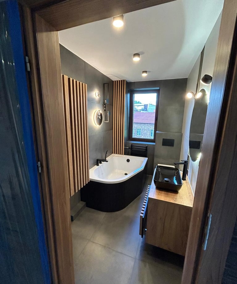 Nowoczesna łazienka z wolnostojącą wanną, drewnianymi panelami na ścianie, czarną umywalką i dużym lustrem.