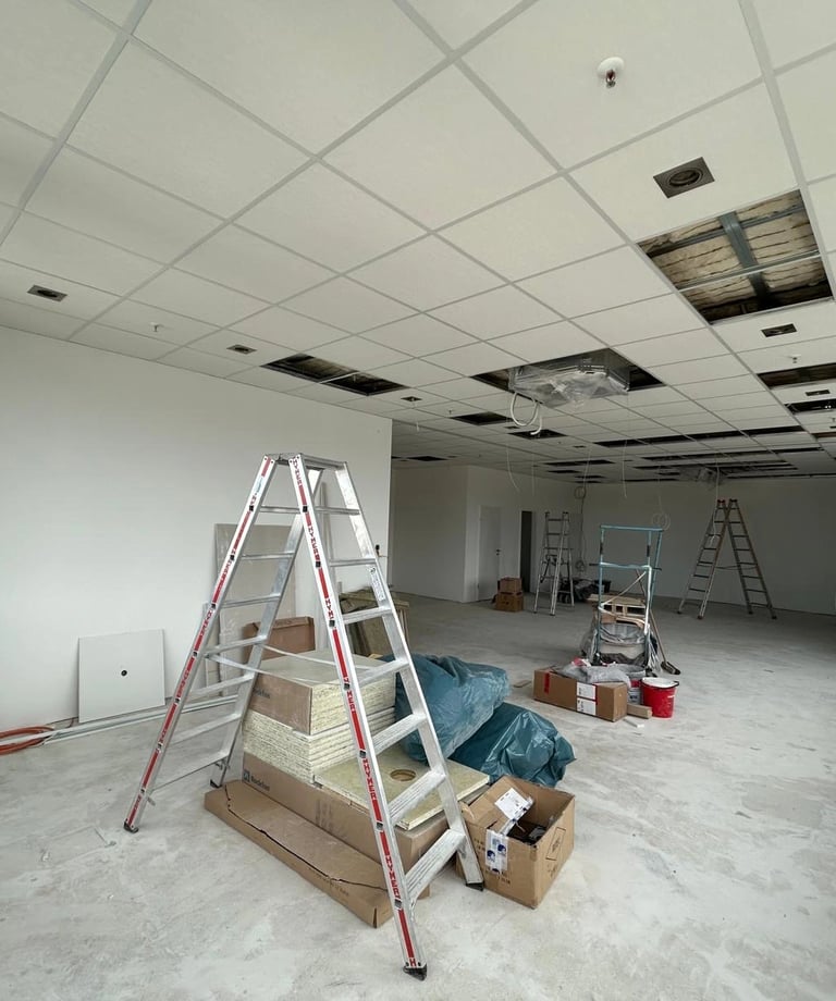 Sufit kasetonowy w trakcie montażu, duża sala z rusztowaniem i czarnymi panelami akustycznymi, płyty sufitowe w układzie pros