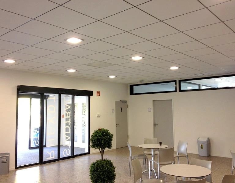 Sufit kasetonowy w biurze, białe kasetony z wbudowanymi lampami LED, minimalistyczne wnętrze z oknami i stolikami.