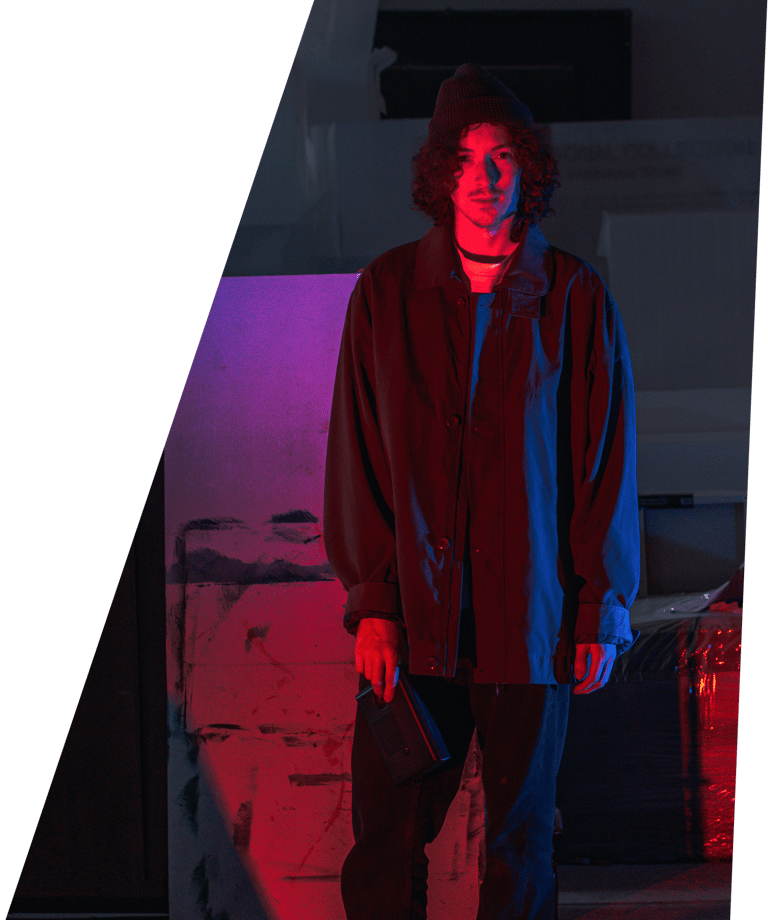 A dark portrait photographic image of In Videcolour lead-songwriter Sam Auckland. Sam is standing, red and blue light on him.