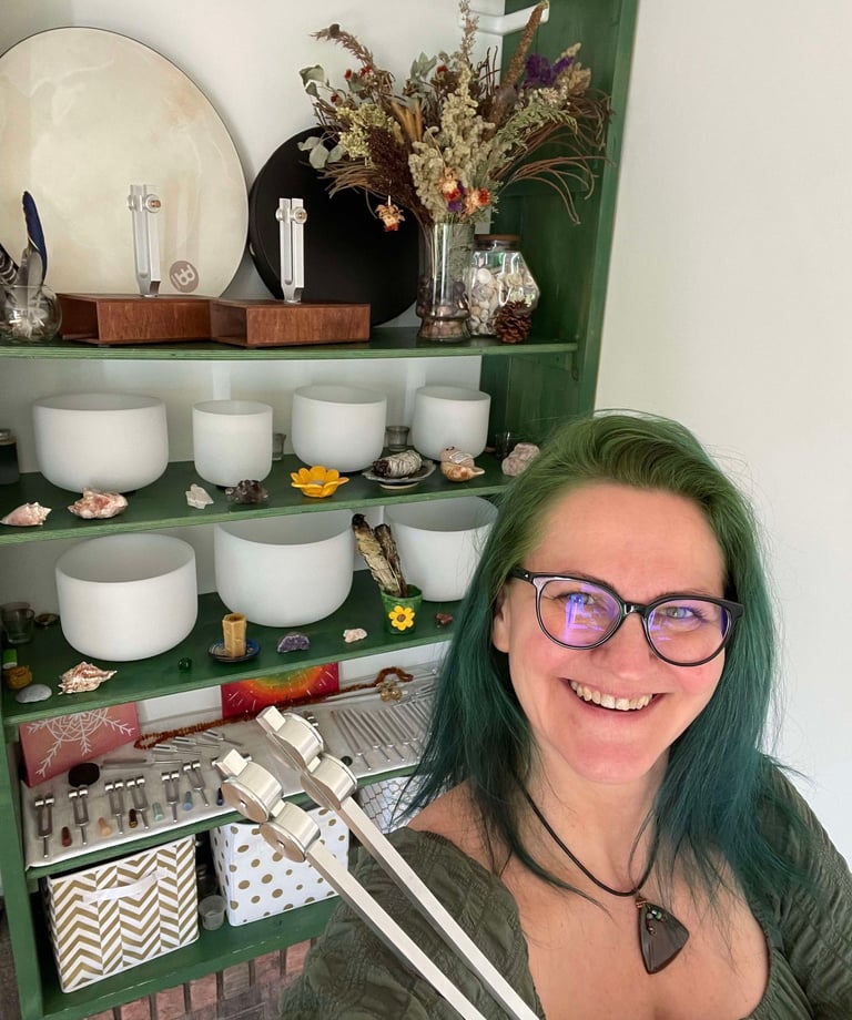 Smiling lady holding a tuning fork and sound bowls behind her