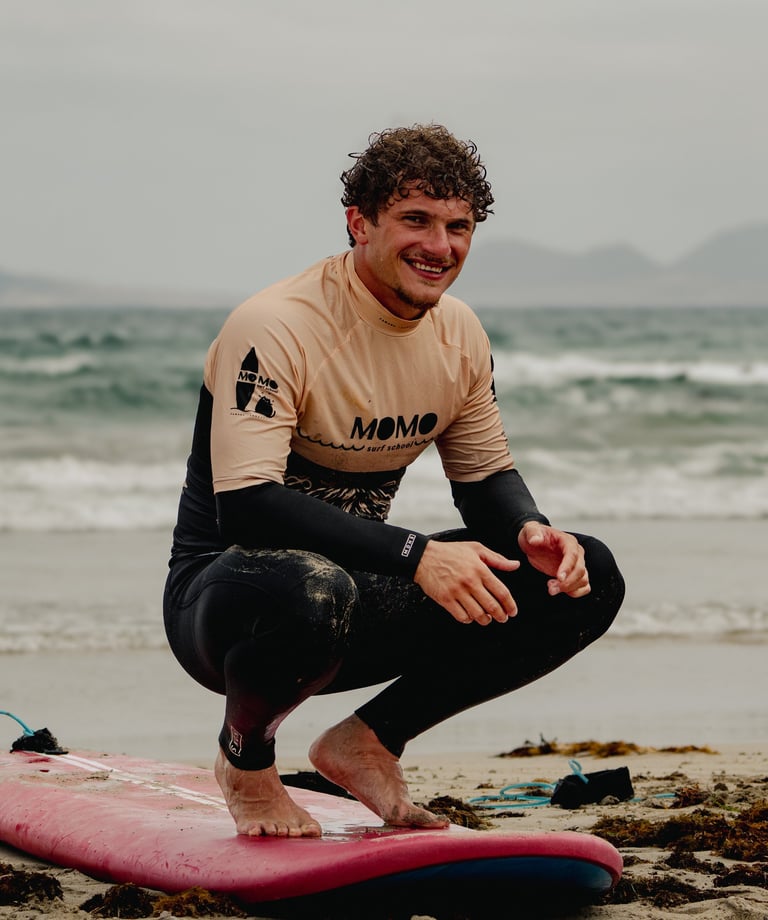 eleve de momo surf school sur sa planche entrain de sourire a la camera