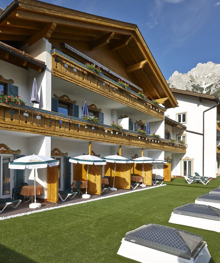Luxury alpine hotel with wooden balconies and green lawn against a mountain backdrop.