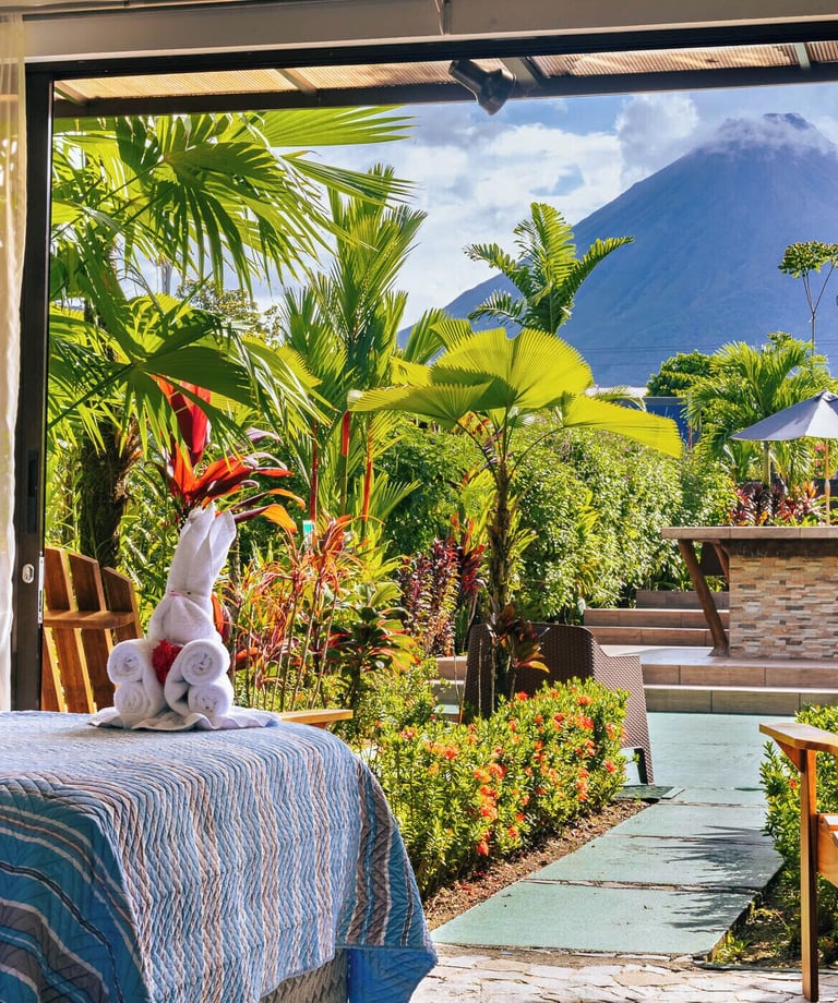 Luxury tropical resort bedroom view of Arenal Volcano through sliding doors with palm trees.