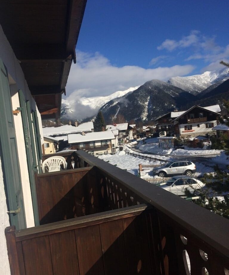 A sunny balcony view of a snowy mountain village with alpine chalets and winter scenery.