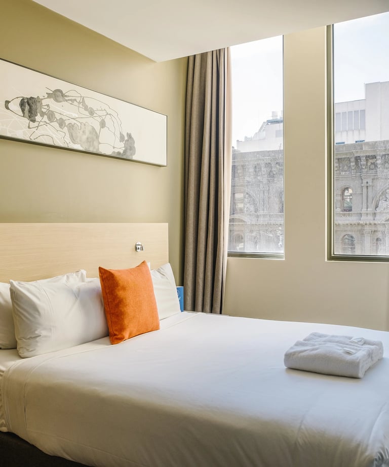 Habitación de hotel moderna con cama queen, sábanas blancas, cojín decorativo naranja