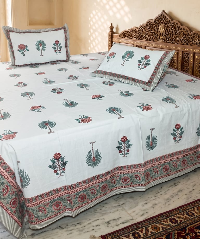 White block print cotton bedsheet with floral and palm tree motifs on a carved wooden bed.