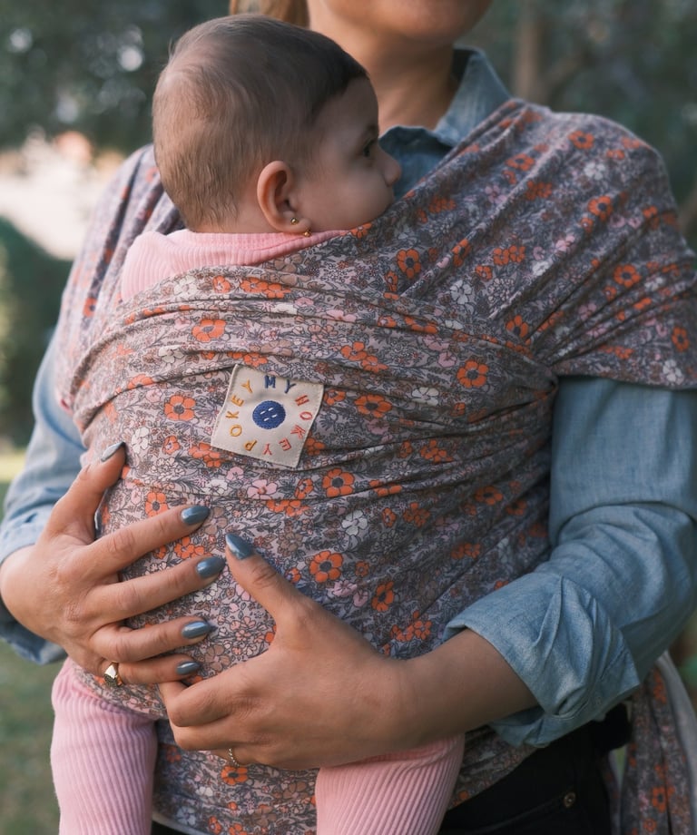 Mother holding her baby in a floral patterned ergonomic baby wrap carrier outdoors.