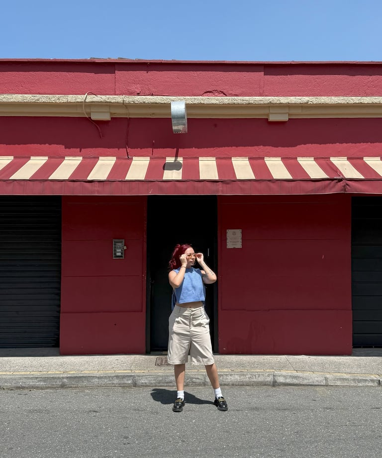 a girl standing in front of a red building. Una niña parada frente a un edificio rojo..