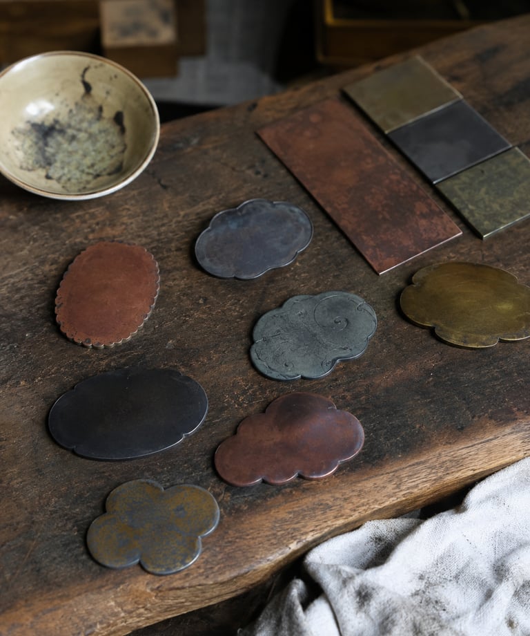 Handcrafted metal tea coasters in cloud and flower shapes on a rustic wooden table.
