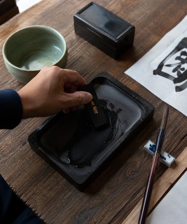 A hand grinding an inkstick on a stone inkwell for traditional Chinese calligraphy.