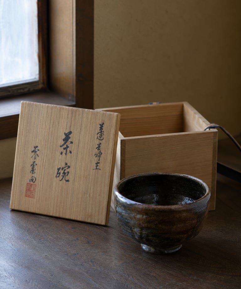 Handmade ceramic Japanese chawan tea bowl next to its traditional wooden storage box.