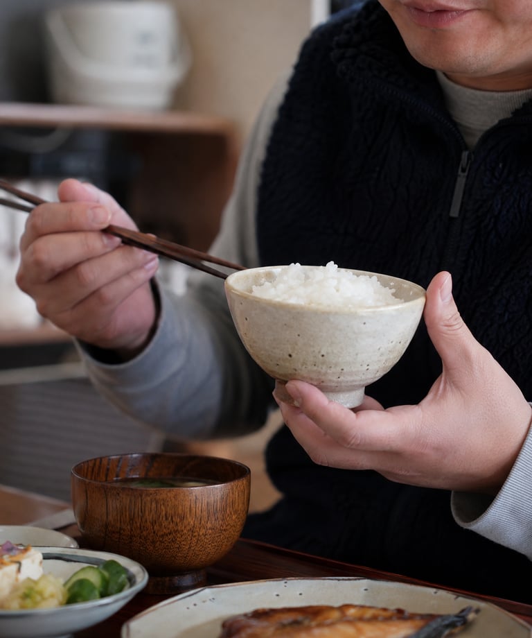 A person eating a traditional Japanese breakfast with white rice, miso soup, and grilled fish.