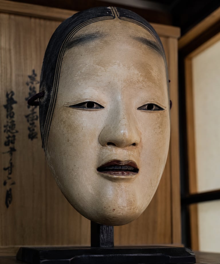 Antique carved wooden Japanese Noh mask of a woman displayed on a stand with a calligraphy box background.